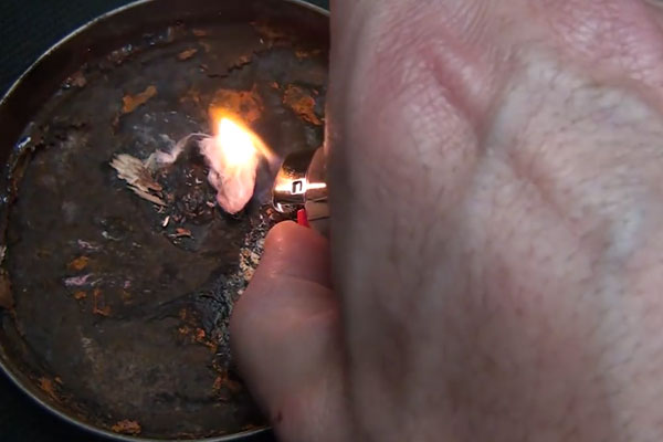 Human hand using a lighter to light some cotton