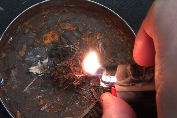 Human hand using a lighter to light tinder