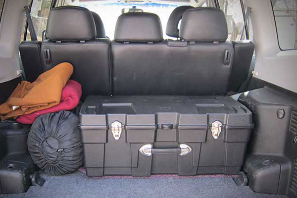 Trunk of a car filled with blankets, a sleeping bag, and a plastic chest