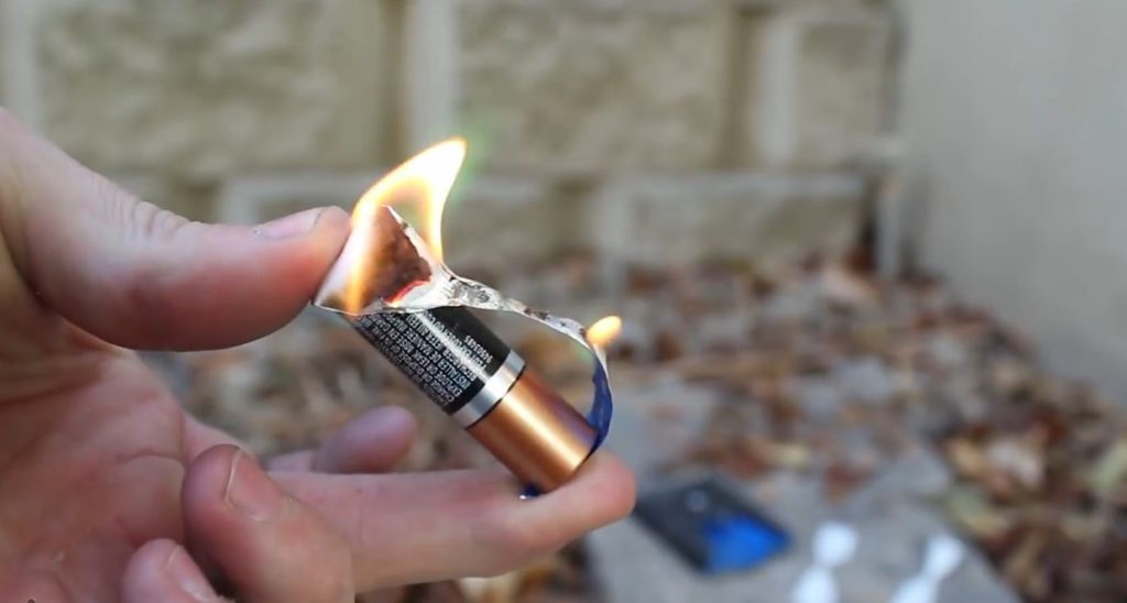 Human hands staring a fire using a AA battery