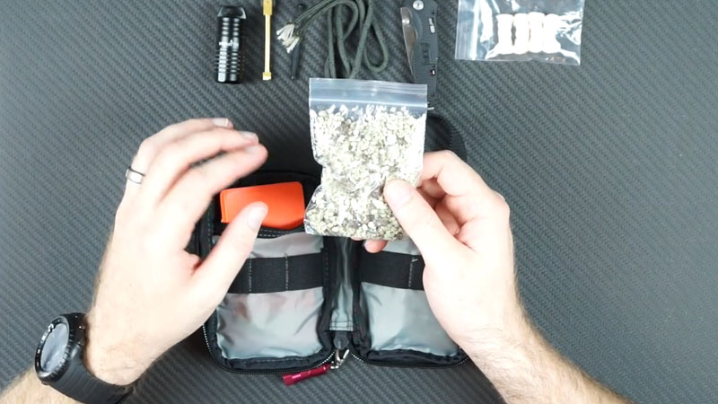 bag of instafire pellets held in right hand over a firestarting kit