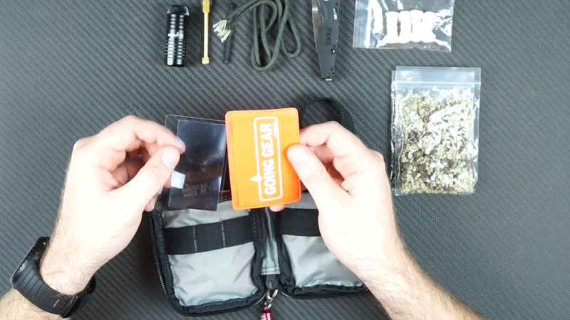 fresnel lens in an orange sleeve held by two hands over a firestarting kit