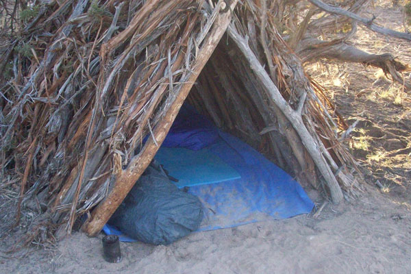 A frame survival shelter with blanket and sleeping bag inside