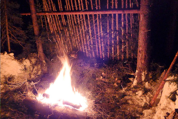Lean-to survival shelter at night with fire