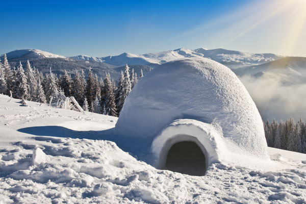 an igloo shelter built in the snow on the side of a mountain with a mountain range in the background