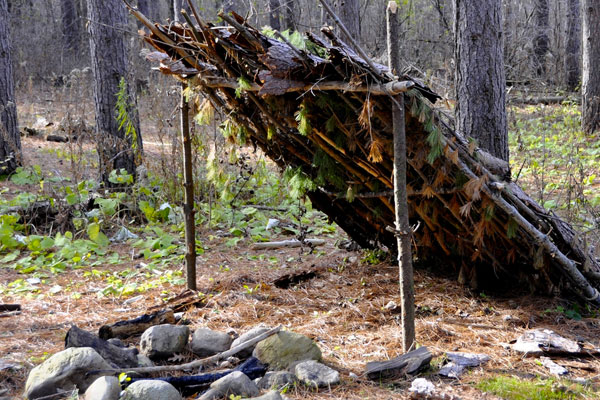 a lean-to type of shelter in the woods with a fire in front of it