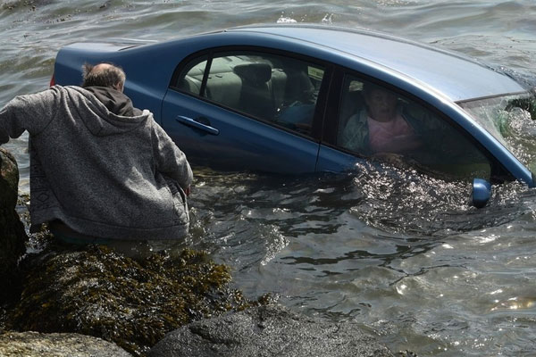 Car sinking in water with man trying to help