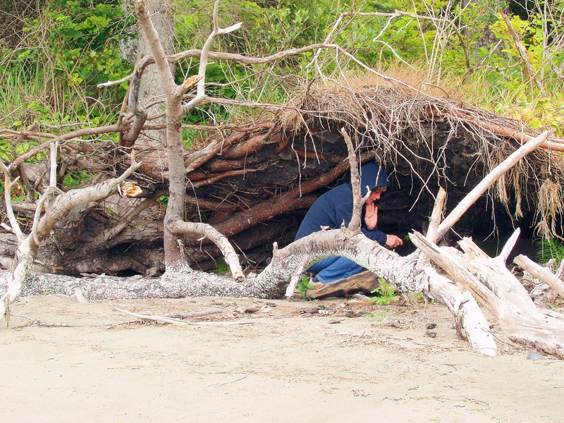 Man underneath a survival shelter built on sand