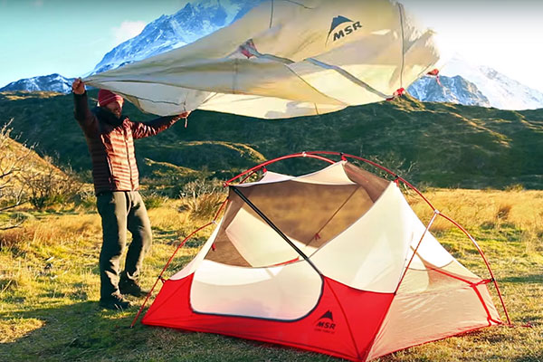 Man putting wind shield on tent in the mountains