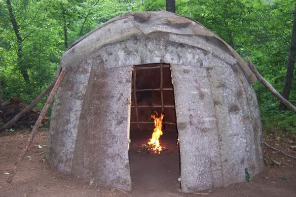a wigwam shelter that looks like a dome with a fire in the middle of it in the forest