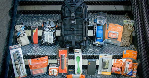 Bug out bag with knives, a water bottle, gloves, socks, silverware, paracord, and a flashlight