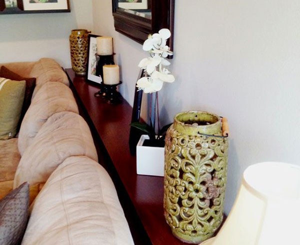 Table behind couch with candles, a lamp, flowers, and a picture frame