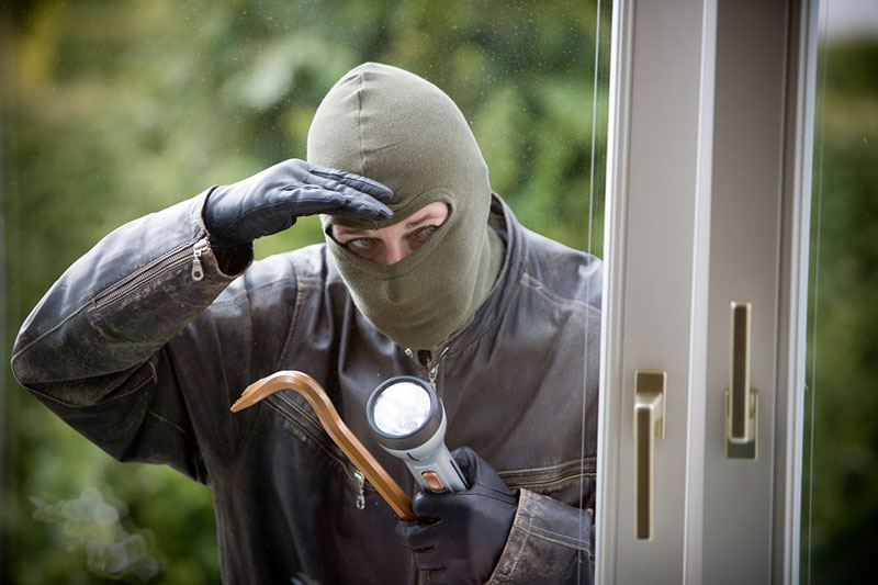 Man looking through window with a mask, crowbar, and flashlight