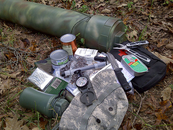 Canned food, water bottle, compass, hat, knife, multi tool, mylar emergency blanket, and a green pipe