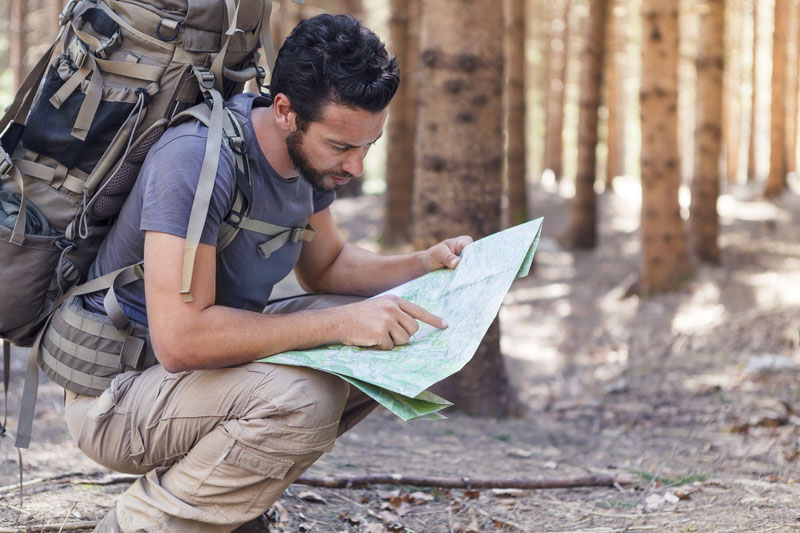 Man with backpack holding and looking at map in the woods