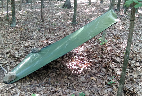 Green tarp lean-to shelter tied to a tree and held by rocks