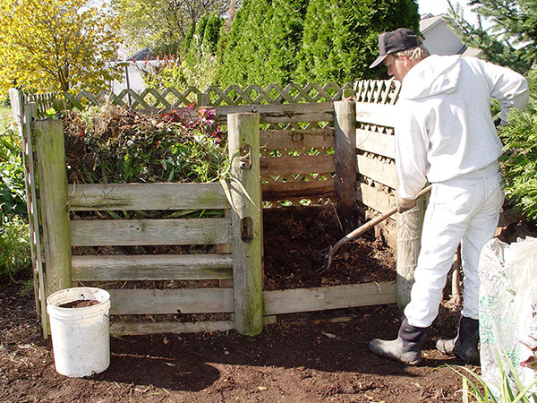 man in gardening clothes turning over compost soil 