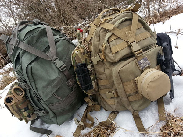 2 backpacks of survival gear sitting in the snow in the woods