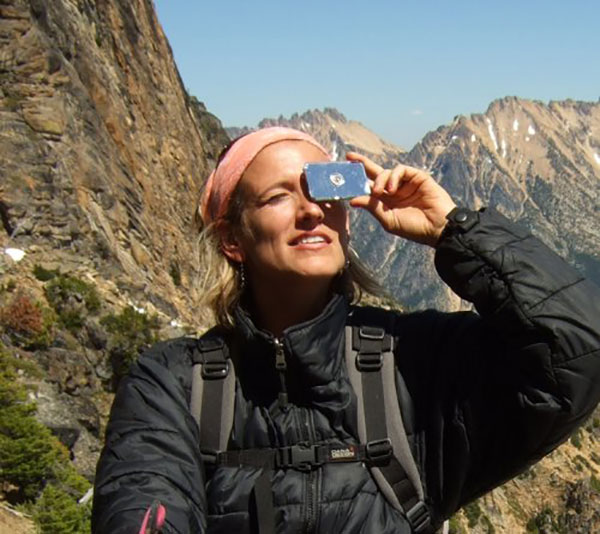 woman holding a signal mirror to her eyes in a mountain range
