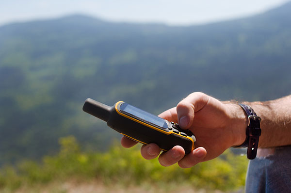 mans hand holding a digital gps device with a mountain in the background