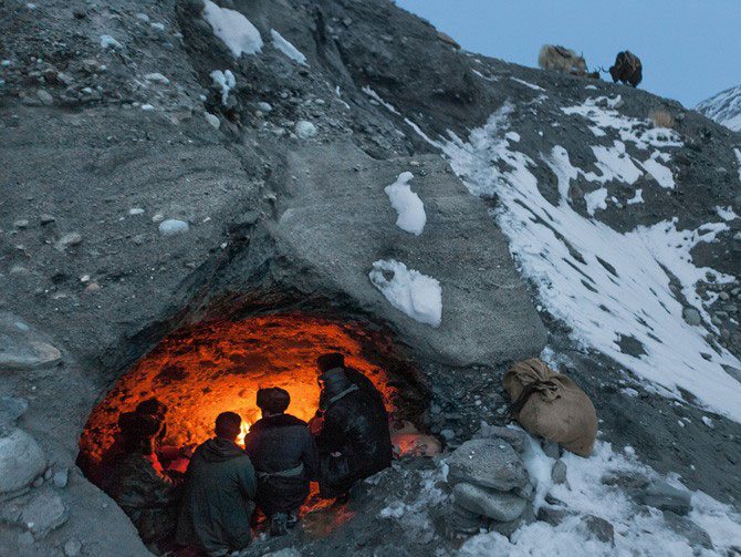 People sitting by a fire inside of a cave in the snowy mountains