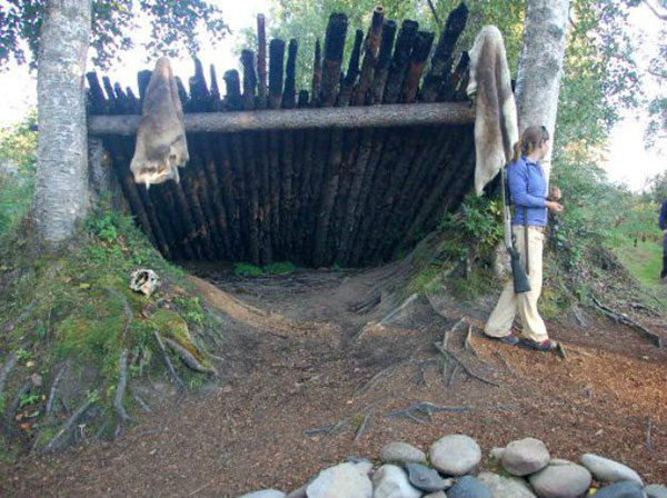 Woman standing by lean to survival shelter built with trees and branches