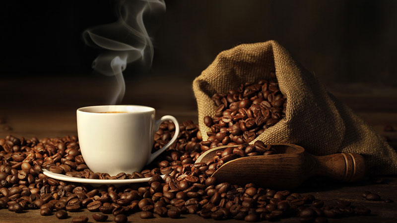 Coffee beans in a cloth sack and a white mug of steaming coffee