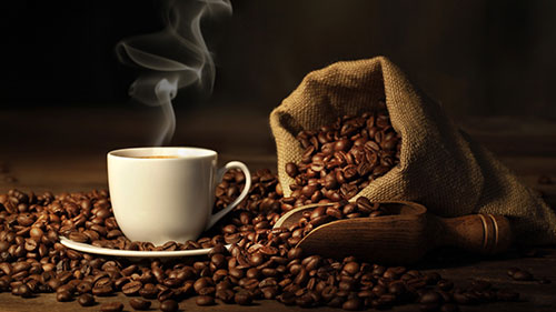 Coffee beans in a cloth sack and a white mug of steaming coffee