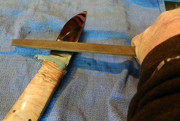 Human hand using a file to sharpen a knife blade