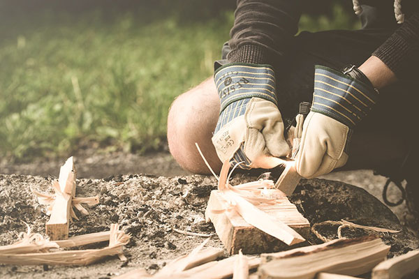 Person in gloves using a ferro rod to start a fire on a log