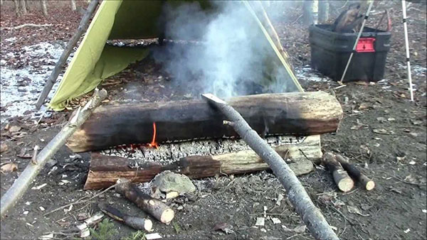 Dying fire smoking with a tarp shelter behind it