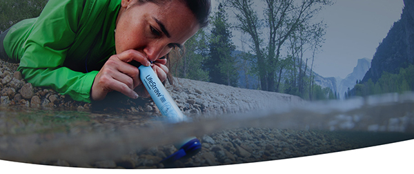 woman drinking water from a stream with a lifestraw