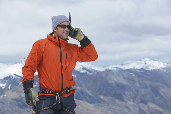 Man in orange jacket using a satellite phone on top of a mountain